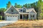 A gray two-story house with white trim at 1155 Shonele Lane in Stem features a double garage, front porch, and manicured shrubs, set on a gravel driveway surrounded by trees and dry grass.