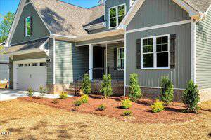 A modern house with gray siding, white trim, and brick accents features a covered porch, black railings, a two-car garage, and a landscaped front yard with small shrubs and mulch.