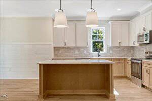 Modern kitchen with light wood cabinets, a center island with a white countertop, stainless steel appliances, white tile backsplash, two pendant lights, and a window above the sink letting in natural light.