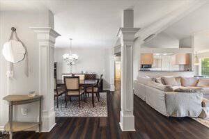 A view of an open-concept living and dining area with dark wood floors, a dining table with six chairs, a chandelier, a beige sectional sofa, and a small entry table with a round mirror on the wall.