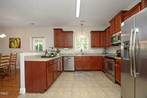A spacious kitchen with wood cabinets, stainless steel appliances, a granite countertop, tiled floor, and a window over the sink. An adjacent dining area with a wooden table and chairs is partially visible.
