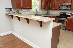 A kitchen with brown cabinets, stainless steel appliances, a double sink, tan countertops, and a raised breakfast bar. A small fish tank sits on the counter and a window is above the sink.