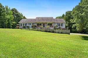 A single-story house at 1855 Bullocksville Park Road, Manson, features a covered front porch and ramp, set on a large grassy lawn surrounded by trees under a clear blue sky.