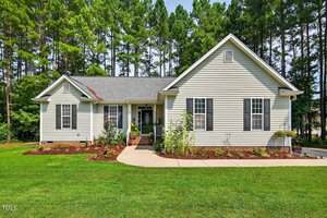 Charming single-story home at 109 N Cinnebar Court, Henderson, with light-colored siding, dark shutters, and a gray roof. A concrete walkway welcomes you to the front door, surrounded by a manicured lawn and tall trees.