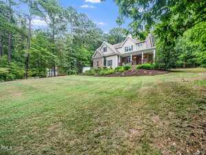 A two-story house with a brick and siding exterior sits at the end of a large, sloped grassy lawn on 3718 Sapphire Court, Franklinton, surrounded by tall trees and dense greenery under a blue sky.