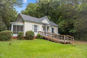 Charming single-story house at 107 Franklin Street, Oxford, with white siding, a gray roof, and blue trim. A wooden wheelchair ramp leads to the porch, surrounded by shrubs and trees, with a grassy lawn in front.
