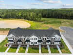 A row of two-story townhouses on 1102 Brookrun Drive in Oxford features identical white facades and gray roofs, seen from above. The homes face a sidewalk and parking area, with a pond and forested area in the background.