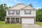 Located at 1841 Fillmore Drive in Creedmoor, this two-story suburban house features white siding, stone accents, black shutters, a covered front porch, and a two-car garage on a grassy lawn surrounded by trees under a blue sky.