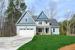 A two-story blue house with white trim, a double garage, and a covered front porch sits on a green lawn with a concrete driveway, surrounded by trees under a partly cloudy sky.