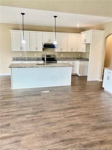 A modern kitchen with white cabinets, stainless steel appliances, granite countertops, a center island with pendant lights overhead, and wood-look flooring.