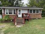 A one-story brick house at 206 1st Street, Oxford, features white siding, red shutters, and a front porch with red railings. Steps lead up to the porch with potted plants, lawn ornaments, and grass in the yard. Trees stand in the background.