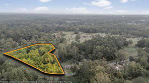 Aerial view of a wooded area in Henderson, outlined in orange to mark the property boundary near 450 Ft Merriman. The property is surrounded by dense trees, with a road and several houses visible nearby under a partly cloudy sky.