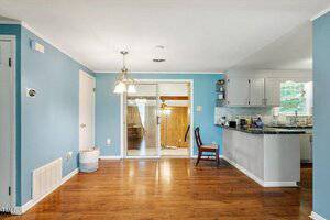 A dining area with hardwood floors, blue walls, and a hanging light fixture. Sliding glass doors lead to another room, and a kitchen with white cabinets and black countertops is visible on the right.