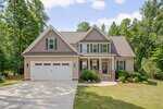 Located at 3800 Watermark Drive in Franklinton, this two-story suburban house features beige siding, stone accents, a front porch, and a two-car garage, nestled among green trees and landscaped shrubbery with an American flag by the entrance.