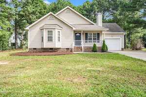 Charming single-story beige house with white trim at 1091 Blackstone Drive, Creedmoor. Features a front porch, attached one-car garage, and small bay window on a large grassy lawn with trees in the background.