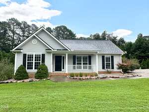 Charming single-story house at 3603 Copper Creek Lane in Franklinton features light gray siding, black shutters, and a covered front porch. The neatly landscaped yard has green grass, small shrubs, a concrete driveway, and trees in the background.