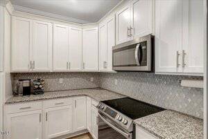 A modern kitchen with white cabinets, granite countertops, a stainless steel microwave, an electric stove, a coffee maker, a knife block, and a patterned tile backsplash.