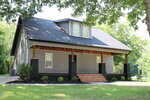 A gray house with a black roof at 405 Sycamore Street in Oxford features a covered front porch with wood accents, black columns, and brown steps, surrounded by grass, small shrubs, and trees in the background.