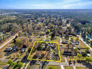 Aerial view of a suburban neighborhood with single-family homes and trees. One property near the center is outlined in yellow to indicate its approximate boundaries. The photo is taken during the daytime.