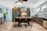 A spacious kitchen at 309 14th Street in Butner features wood cabinets, a central island with four chairs, stainless steel appliances, a light blue tile backsplash, and ample natural light from multiple windows. Decor and plants add charm throughout.