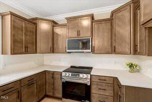 Modern kitchen with light brown wooden cabinets, white countertops, a stainless steel stove with oven, a built-in microwave, and a small vase of yellow flowers on the counter.