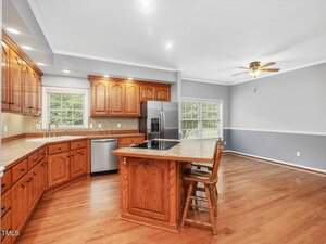 Spacious kitchen with wood cabinets, stainless steel appliances, an island with a cooktop and seating, hardwood floors, and an adjacent dining area with large windows and a ceiling fan.