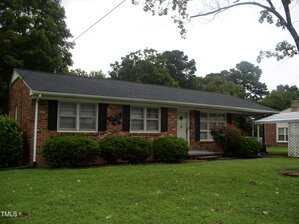 A single-story brick house with black shutters and a dark roof sits on a well-kept lawn at 546 Sagefield Drive in Henderson. Bushes line the front of the house, with trees in the background and part of a white carport visible on the right.