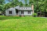 A gray, single-story house at 703 Forrest Lane in Creedmoor features a small front porch, multiple windows, a brick chimney, and an adjacent carport, all set on a grassy lawn with trees in the background.