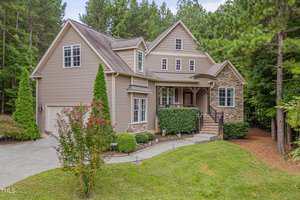 Charming two-story house at 1633 Carriage Drive, Franklinton, with beige siding and stone accents. Surrounded by trees and shrubs, it features a covered porch with railing and well-maintained landscaping.