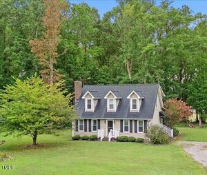 A two-story house at 75 Fairview Drive in Henderson features dormer windows, a brick chimney, and a front porch, surrounded by a green lawn and tall trees in the background under a blue sky.