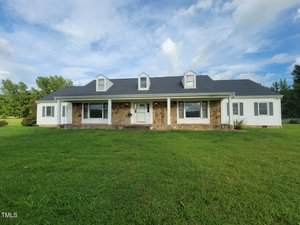 A single-story Oxford house with stone and white siding, three dormer windows on the roof, a covered front porch, and a large green lawn at 4512 Belltown Road under a partly cloudy sky.