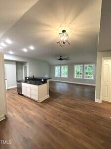 Open-concept living space with wood flooring, a kitchen island with a dark countertop, modern ceiling lights, large windows, and a ceiling fan. Neutral walls and white trim complete the interior.
