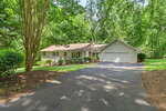 Charming single-story Oxford home at 5204 Tabbs Creek Lane featuring a front porch, attached three-car garage, and dormer windows, nestled among trees and greenery with a paved driveway leading up to the residence.