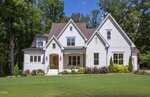 A large modern white house with a gabled roof at 3901 Laurel Creek Lane, Wake Forest, featuring a front porch and well-maintained lawn, surrounded by trees and landscaped shrubs on a sunny day.
