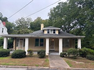 Located at 111 W Jennette Avenue in Henderson, this charming one-story house features a covered front porch, beige exterior with white columns, a dark roof, and is surrounded by front yard bushes and trees under a cloudy sky.