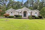 Charming single-story brick house at 139 Ridge Road in Butner, featuring arched windows, white trim, and a covered entry with columns. Enjoy a manicured lawn, shrubs, and tall trees providing a picturesque backdrop.