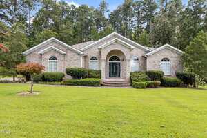 Charming single-story brick house at 139 Ridge Road in Butner, featuring arched windows, white trim, and a covered entry with columns. Enjoy a manicured lawn, shrubs, and tall trees providing a picturesque backdrop.