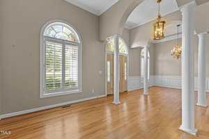 Spacious entryway and dining area with hardwood floors, large arched windows with white shutters, double front doors, high ceilings, white columns, and gold chandeliers.