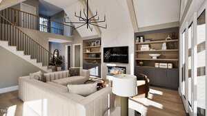A modern living room with vaulted ceiling, beige sectional sofa, round coffee table, wall-mounted TV above a fireplace, built-in shelves, and large windows letting in natural light. A staircase is visible in the background.