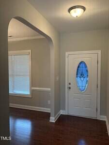 A view of a home's entryway featuring a white door with an oval glass insert, light gray walls, white trim, wood flooring, a window with blinds, and a ceiling light fixture.