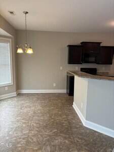 A kitchen area with brown tile flooring, beige walls, dark wood cabinets, granite countertops, and a breakfast bar. A hanging light fixture is above a small dining space near a window with closed blinds.