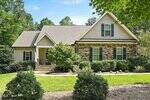A single-story suburban house at 1270 Silky Willow Drive in Wake Forest features tan siding, stone accents, black shutters, and a gabled roof. Shrubs, small trees, and a manicured lawn with a concrete path enhance its inviting curb appeal.
