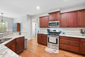 A modern kitchen with dark wood cabinets, granite countertops, stainless steel gas stove and microwave, white subway tile backsplash, and hardwood floors. There are a few kitchen items and mats on the floor.