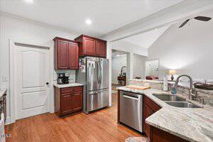 A modern kitchen with stainless steel appliances, dark wood cabinets, a coffee maker, granite countertops, and a double sink overlooking an open living area with wood floors.