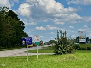A roadside scene shows signs for Henderson, a Purple Heart City, a "DO NOT LITTER" sign, and a directional sign for I-85. There are businesses and trees along the road under a partly cloudy sky.