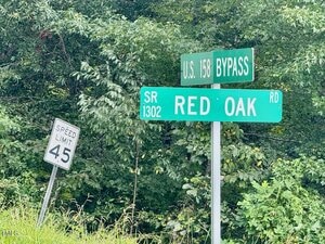 Two green road signs mark the intersections of U.S. 158 Bypass and SR 1302 Red Oak Road. A white speed limit sign beside them shows a limit of 45 mph. Dense green foliage is in the background.