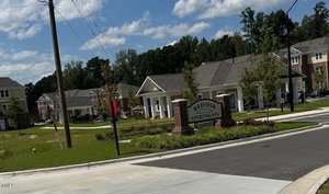 A sign reading "Red Oak Apartments" stands at the entrance to a residential apartment complex with multiple two-story buildings, a lawn, and surrounding trees under a partly cloudy sky.