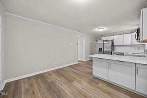 A modern kitchen with white cabinets, stainless steel appliances, and a white subway tile backsplash. The floor has a wood-like finish, and the adjacent wall is plain and light-colored.