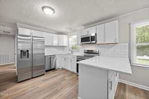 Modern kitchen with white cabinets, stainless steel appliances, subway tile backsplash, wood-style flooring, and a window letting in natural light. A peninsula counter extends into the room on the right.