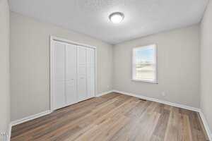 Empty room with light beige walls, a ceiling light fixture, a window with white trim, a closed white double-door closet, and wood-look laminate flooring.